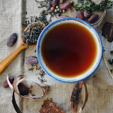 Black tea in a white mug on a cream placemat surrounded by tea leaves and other decor